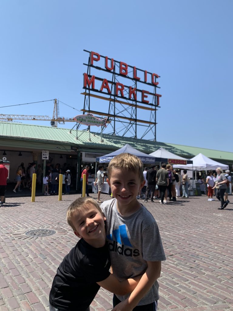 Two boys adventuring in front of the public market sign.