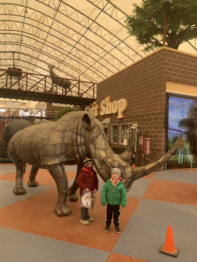 Two adventurous kids standing in front of a rhino statue.