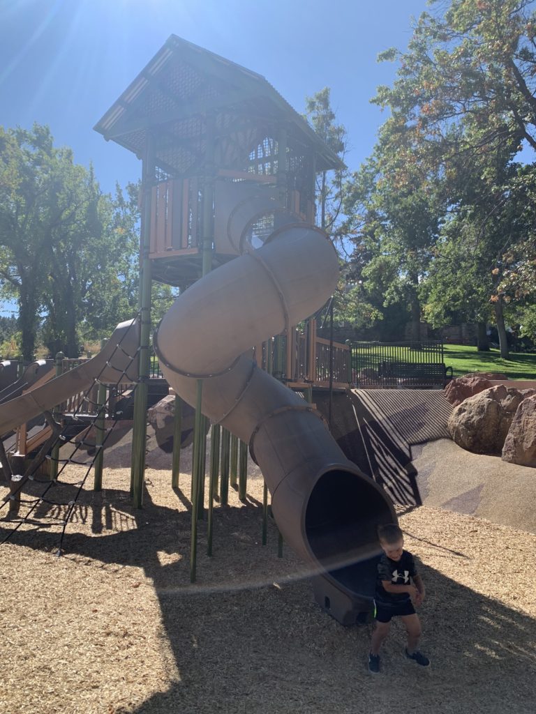 A family boy standing in front of a playground with a slide.