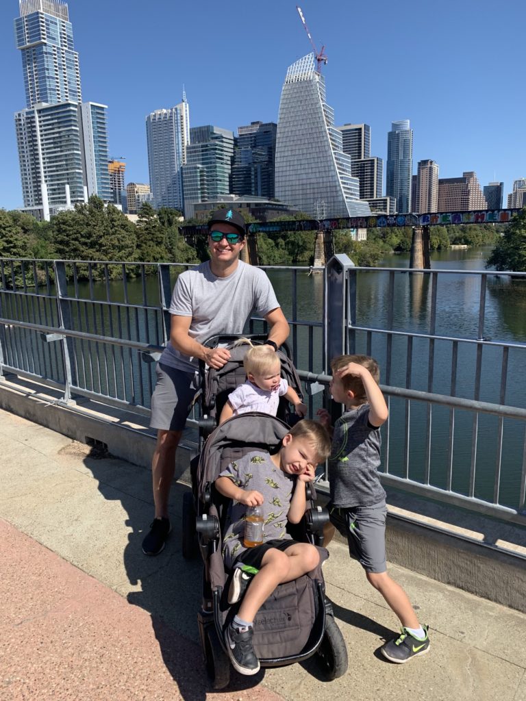 A family with a stroller and two children in front of a city skyline in Austin, TX.