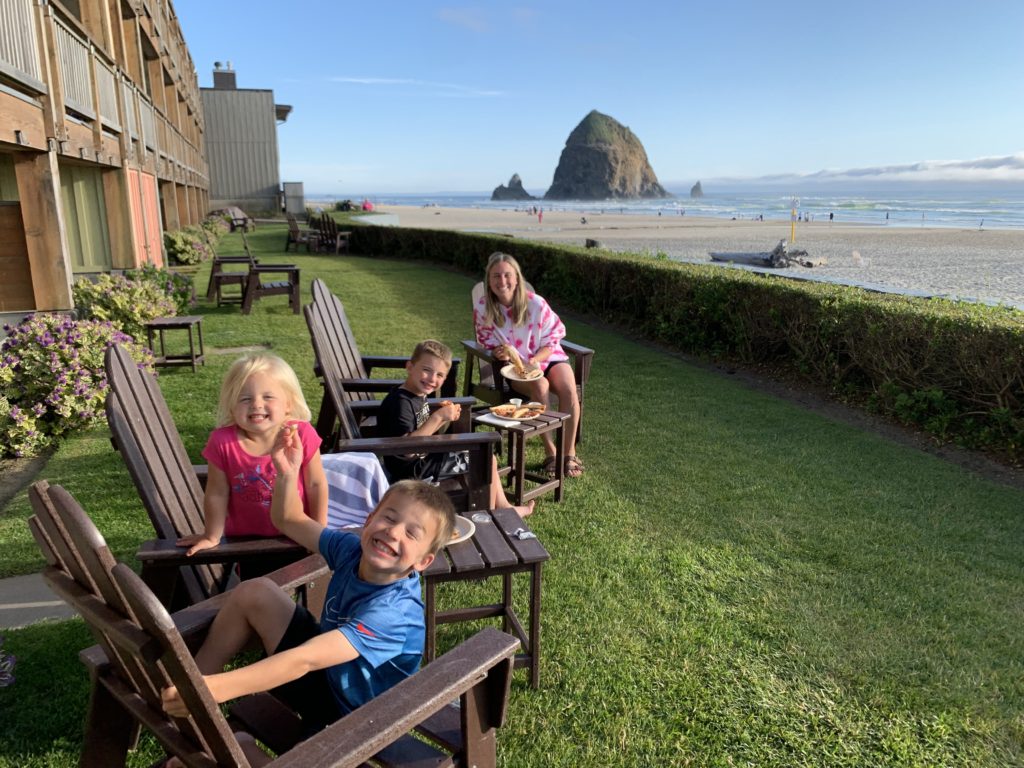 A family sits on a lawn chair in front of a beach, enjoying their travel adventure on a Pacific Northwest Road Trip.