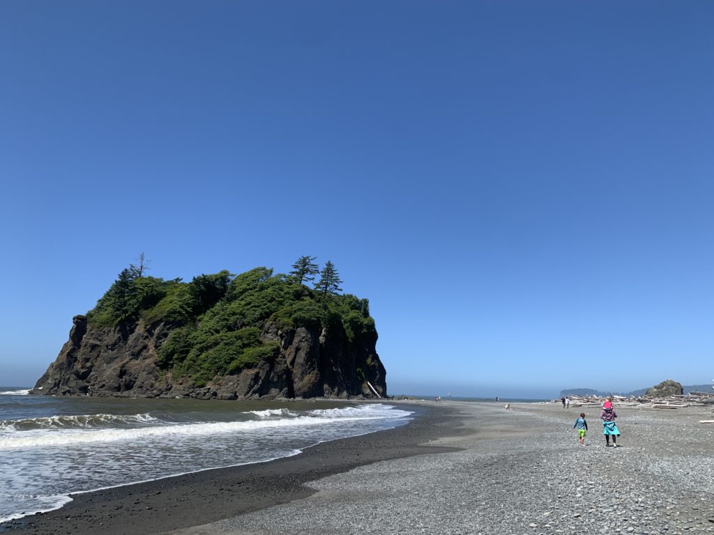 Two people on a travel adventure walking on a beach near an island.