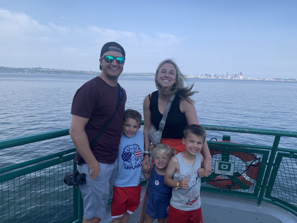 A family with kids is posing for a picture on a ferry during their travel on their Pacific Northwest Road Trip.