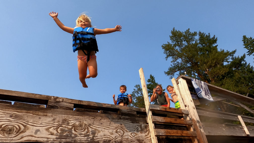 A family adventure where kids jump off a wooden platform in life jackets.