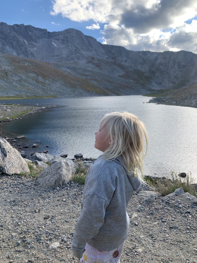 A little girl on a family adventure, looking out over a lake at Mount Blue Sky, Mount Evans. 