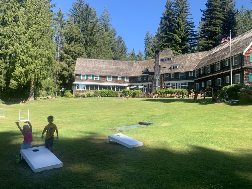 Two kids playing cornhole in front of a house.