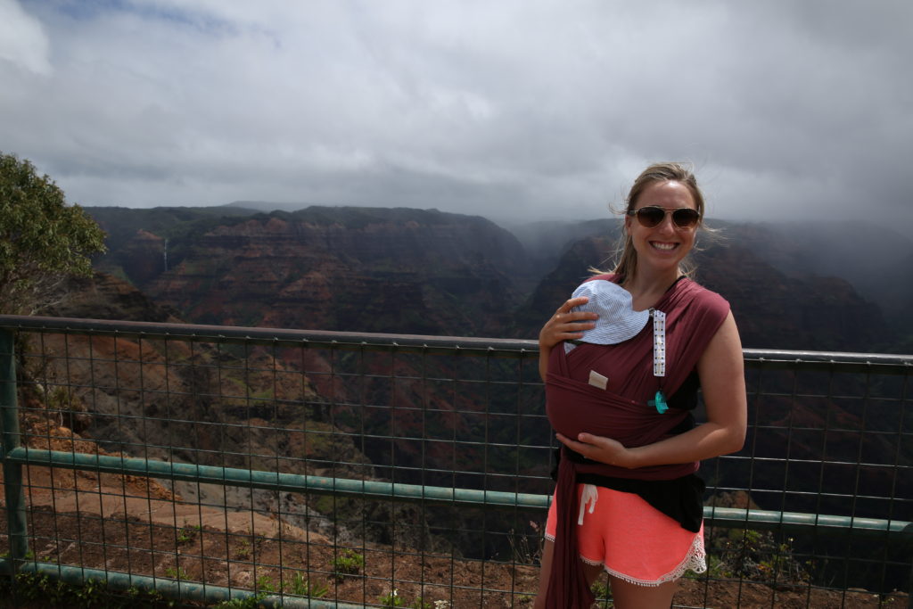 A woman holding a baby in a sling while embarking on an adventurous journey near a cliff.  A fun adventure you can do traveling with your baby!