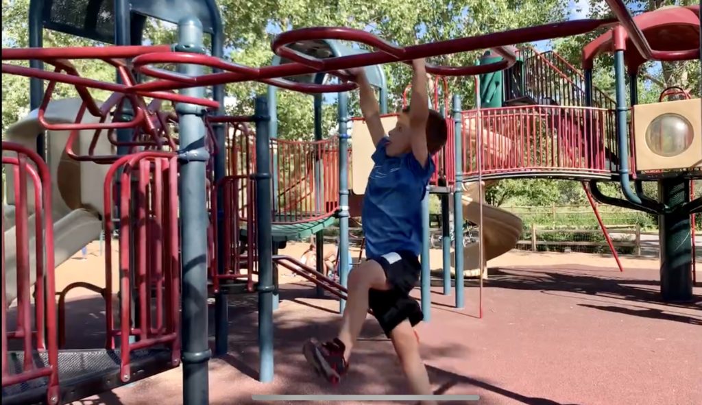 A family boy is doing the monkey bars on a playground at Lions Park in Golden.  One of the best things to do in Golden with kids.