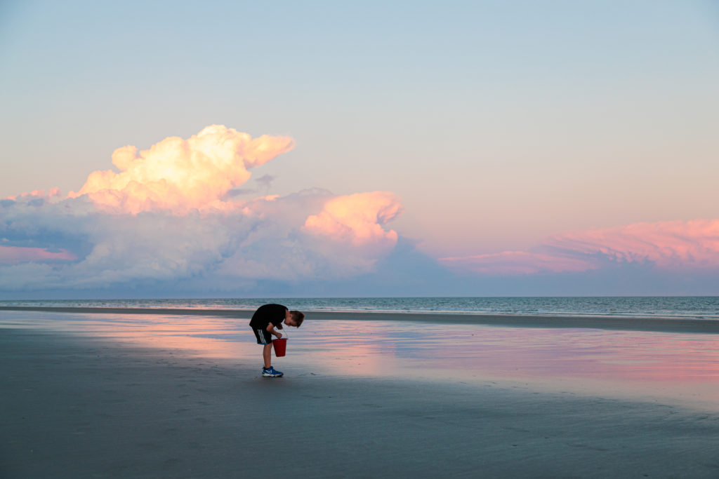 A child standing on a beach with a bucket.