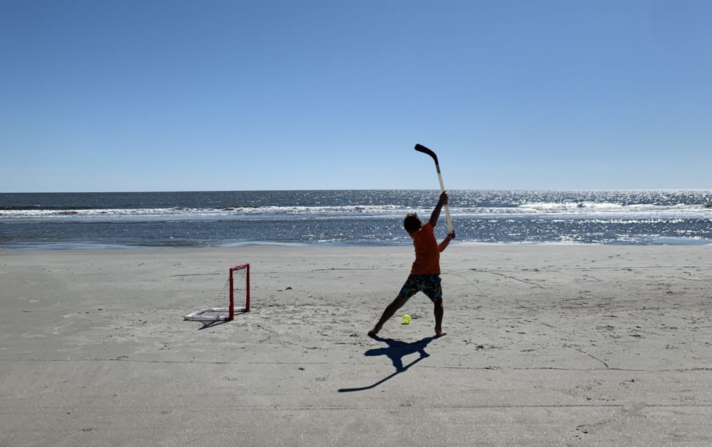 A kid is playing a game of hockey on the beach.