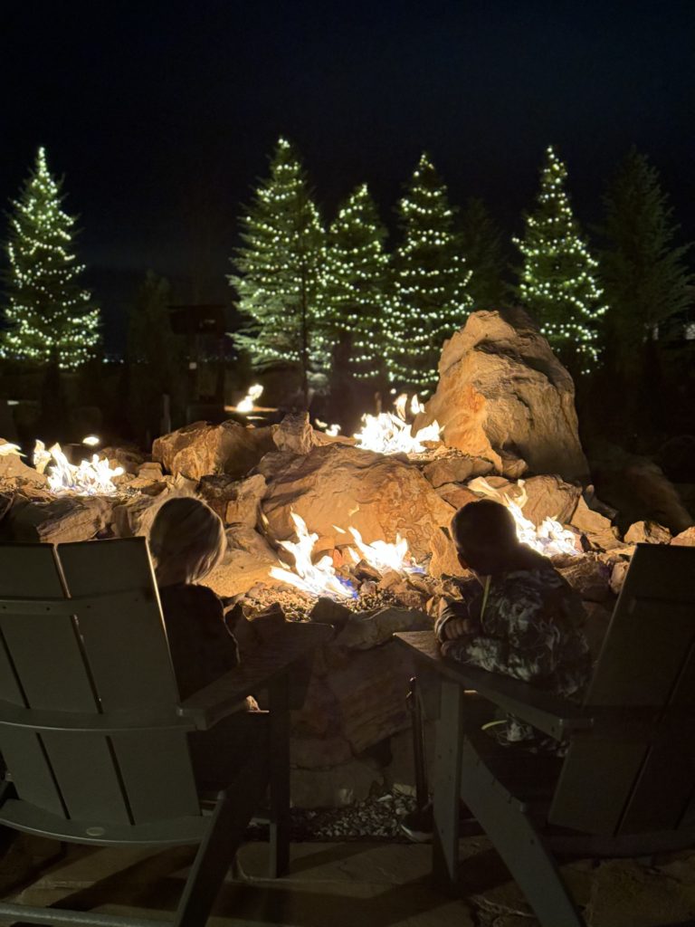 A group of people sitting around a fire pit at night.