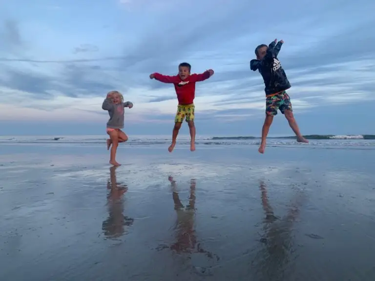 Three children jumping in the air at the beach.