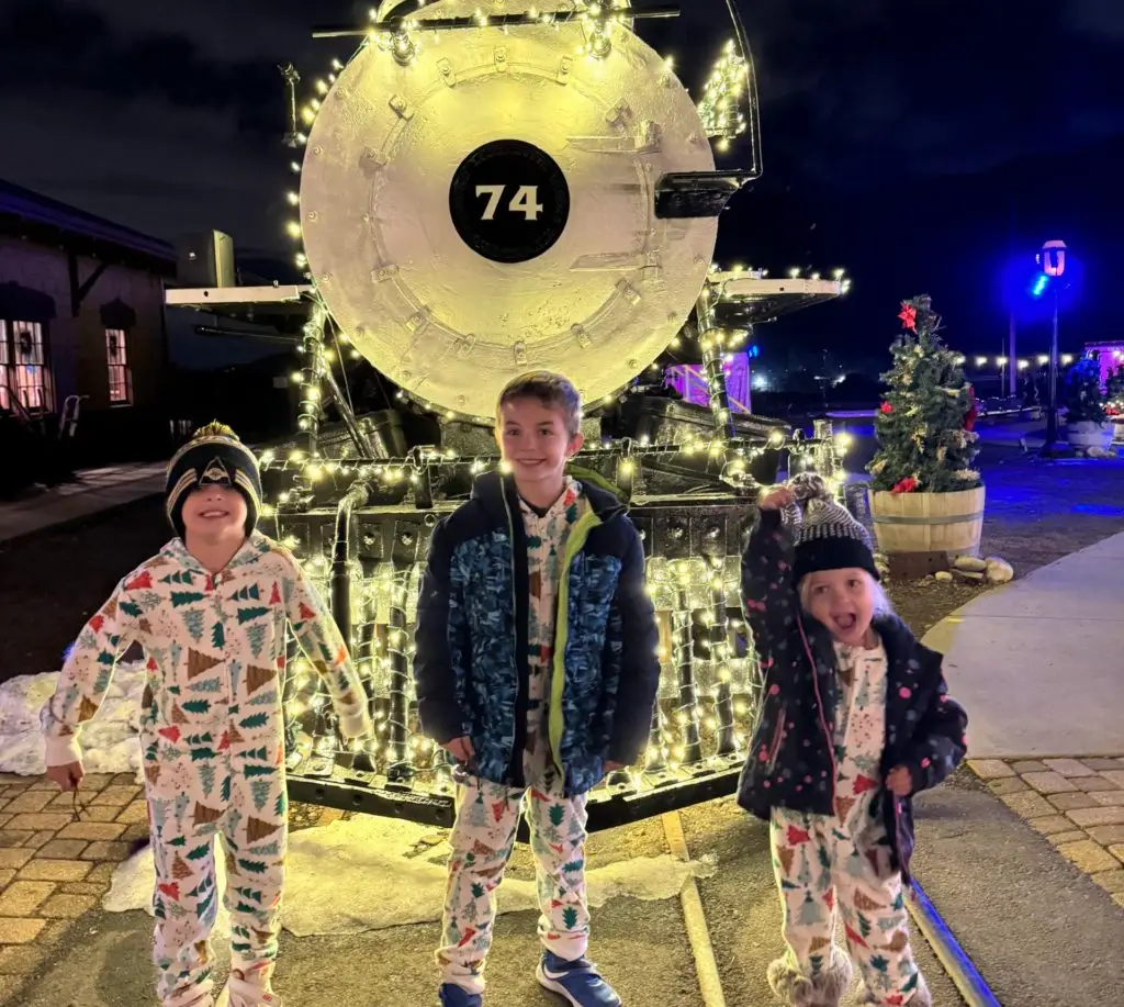 Three children in pajamas standing in front of a train.