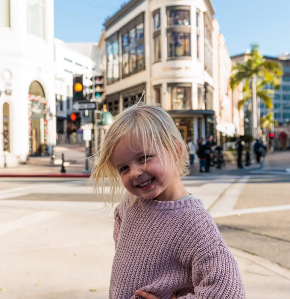 A little girl in a pink sweater standing on a street corner.