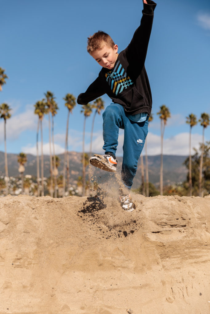 A young boy jumping over a sand pit in front of palm trees. Beaches in Santa Barbara With Kids