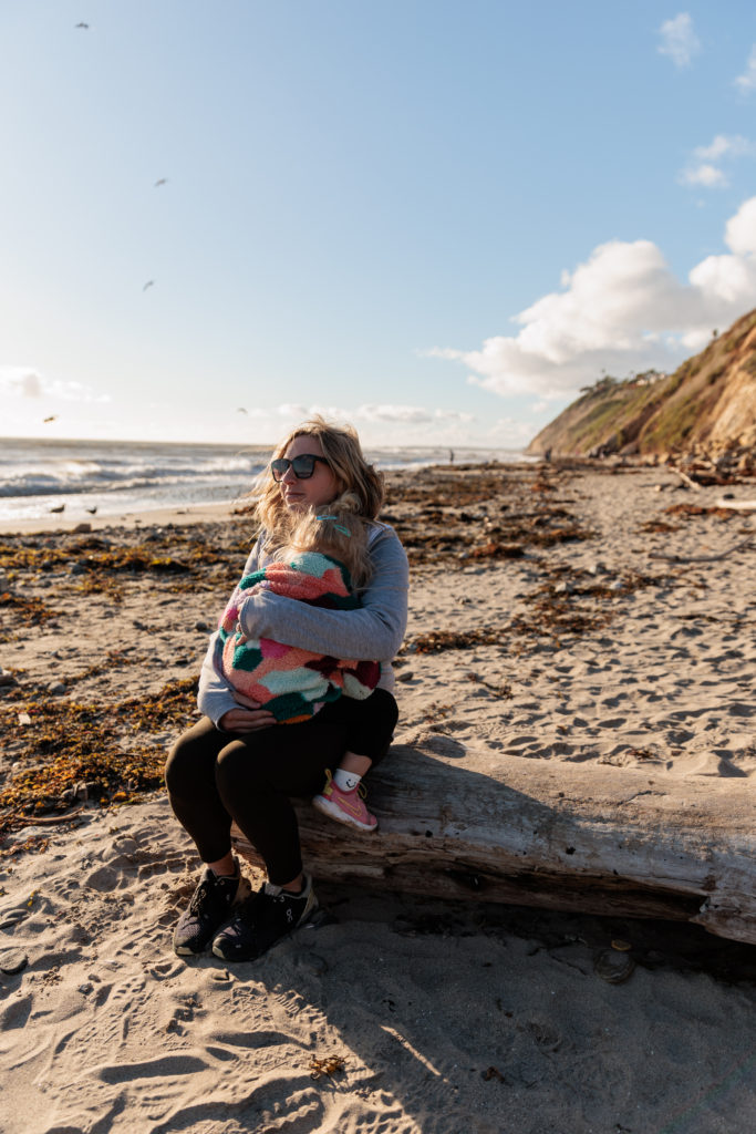 A woman sitting on a log on the beach. Beaches in Santa Barbara With Kids