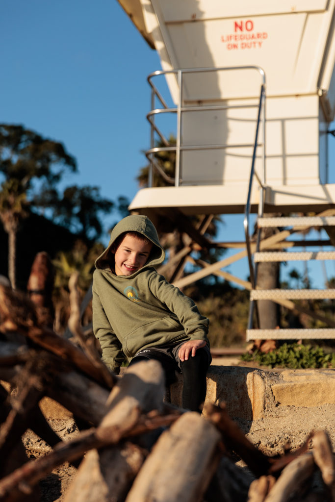 A young boy sitting on a log next to a lifeguard tower. Beaches in Santa Barbara With Kids