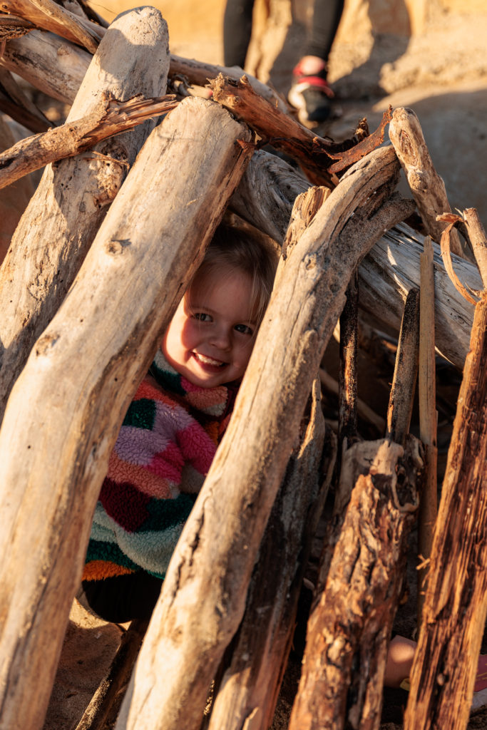 A little girl peeking out of a pile of logs. Beaches in Santa Barbara With Kids