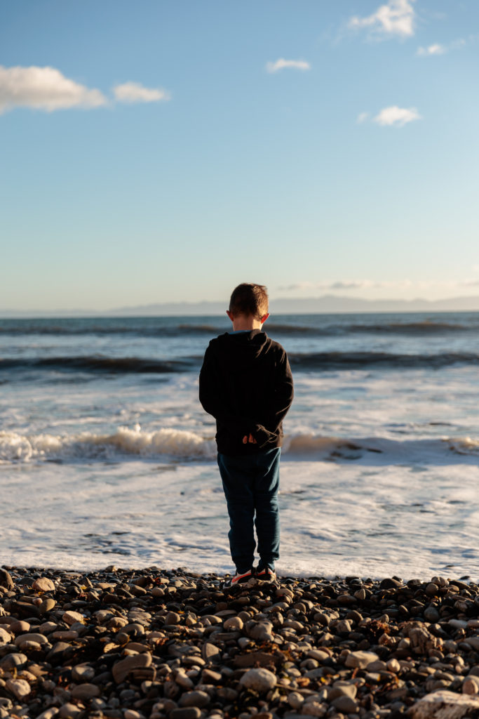 A boy is standing on a rocky beach looking at the ocean. Beaches in Santa Barbara With Kids