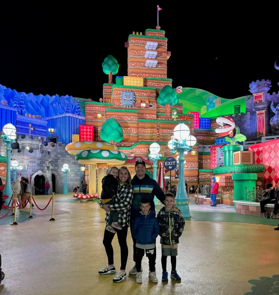 A family is posing in front of a disney world at night.