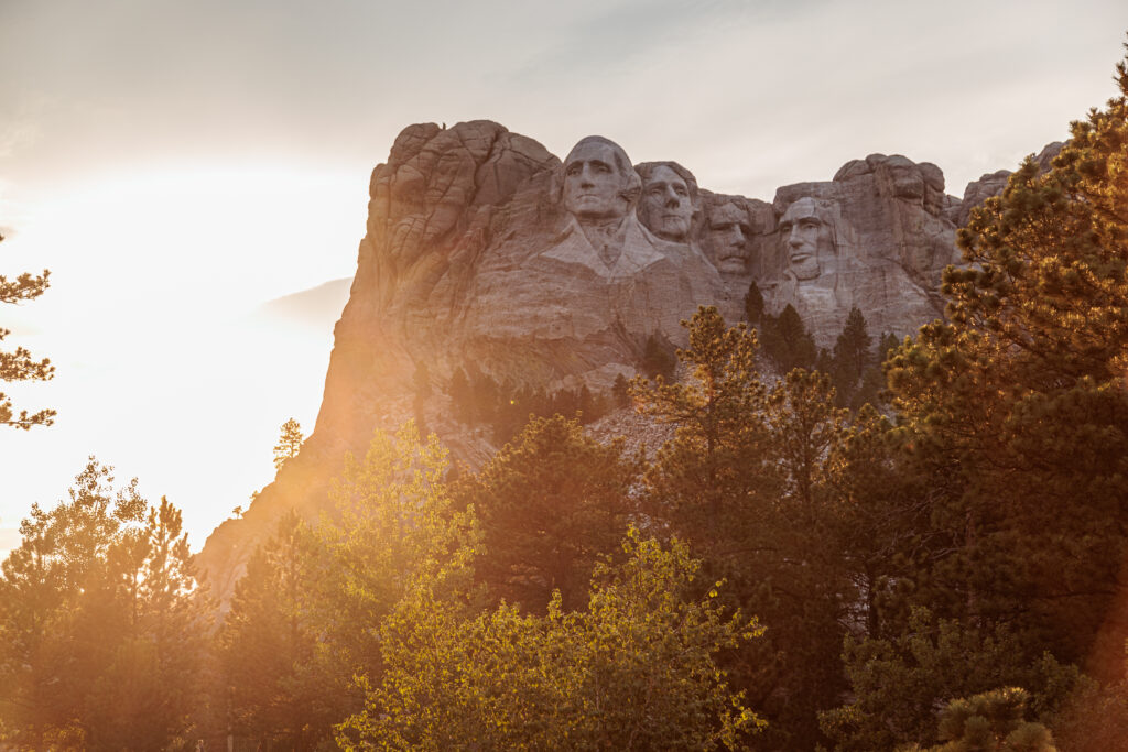 Mount Rushmore with carved faces of four U.S. presidents at sunset, surrounded by trees.