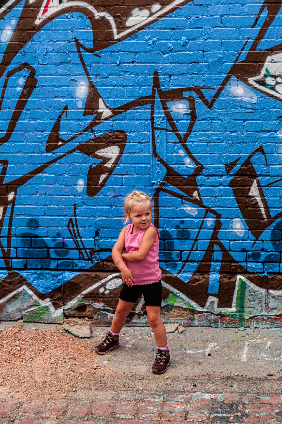 Child in a pink tank top and black shorts posing in front of a blue graffiti-covered wall.  Free things to do in Rapid City with kids.