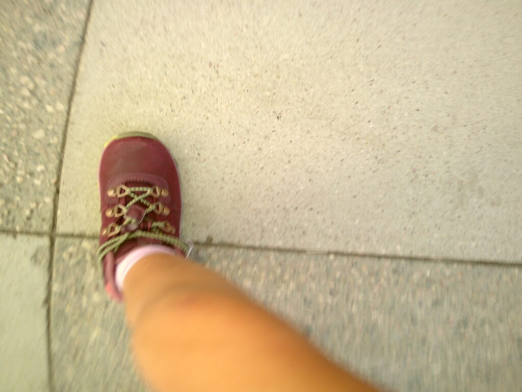 Blurry image of a person walking on a sidewalk, showing one foot in a red shoe stepping forward. Camp Snap Discount Code