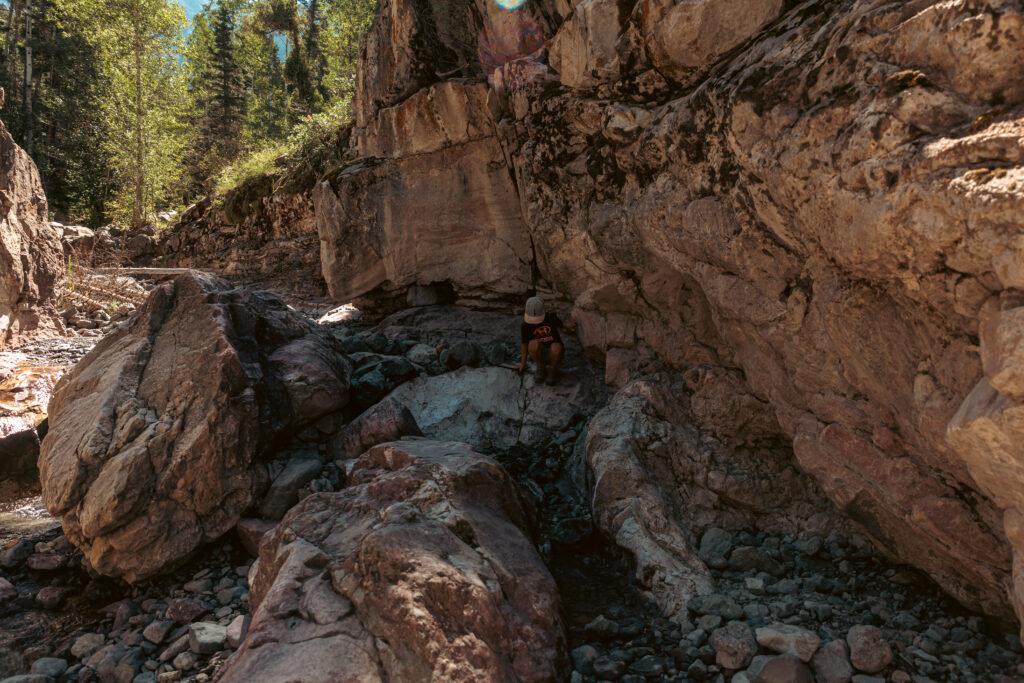 Person hiking and sitting on rocks in a rocky canyon with sunlight shining through trees. 2 days in Ouray with kids.