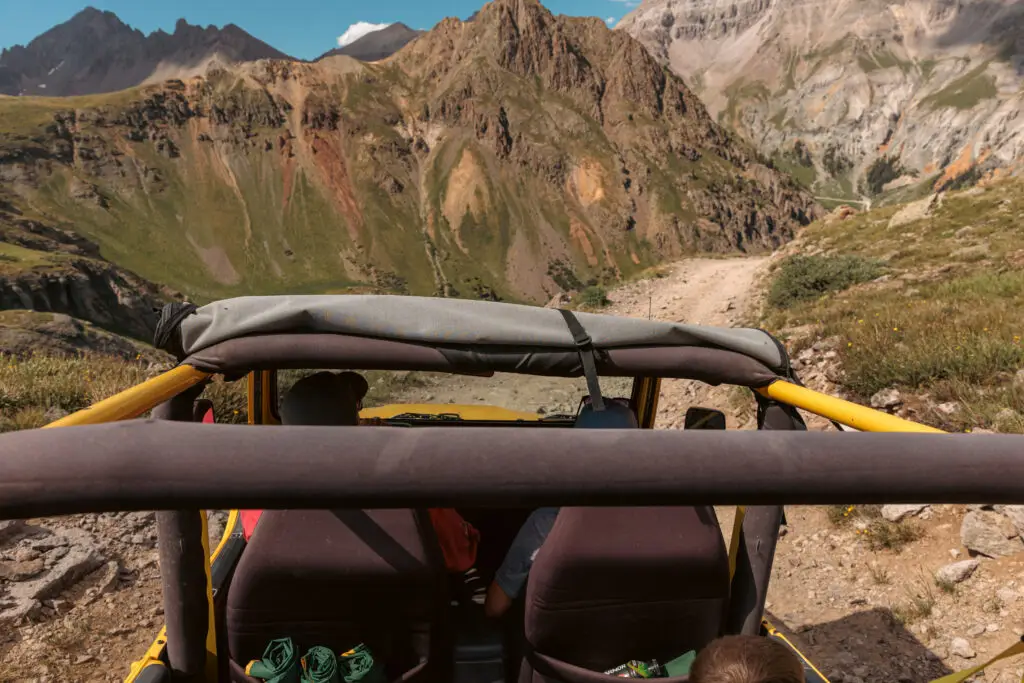 View from the backseat of a jeep driving on a rugged mountain trail, surrounded by steep rocky hills and clear skies. 2 days in Ouray with kids.