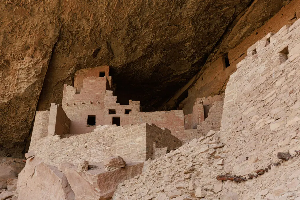 Explore the ancient cliff dwellings of Mesa Verde with kids, where steep rock faces host multiple rooms and windows, all meticulously crafted from light brown stones.