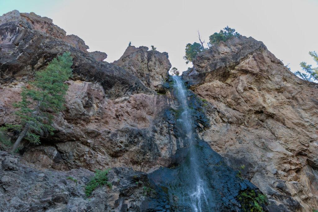 The waterfall cascades down a rocky cliff, surrounded by sparse greenery and a clear sky—a perfect scene for families exploring the natural beauty of Pagosa Springs with kids.